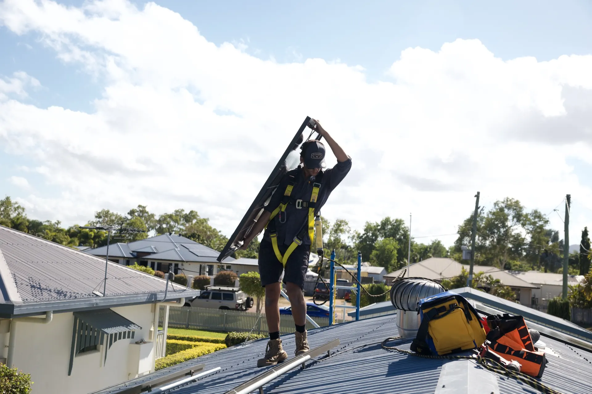 An installer in a harness carrying a new dual-glass solar panel across the Kelso roof