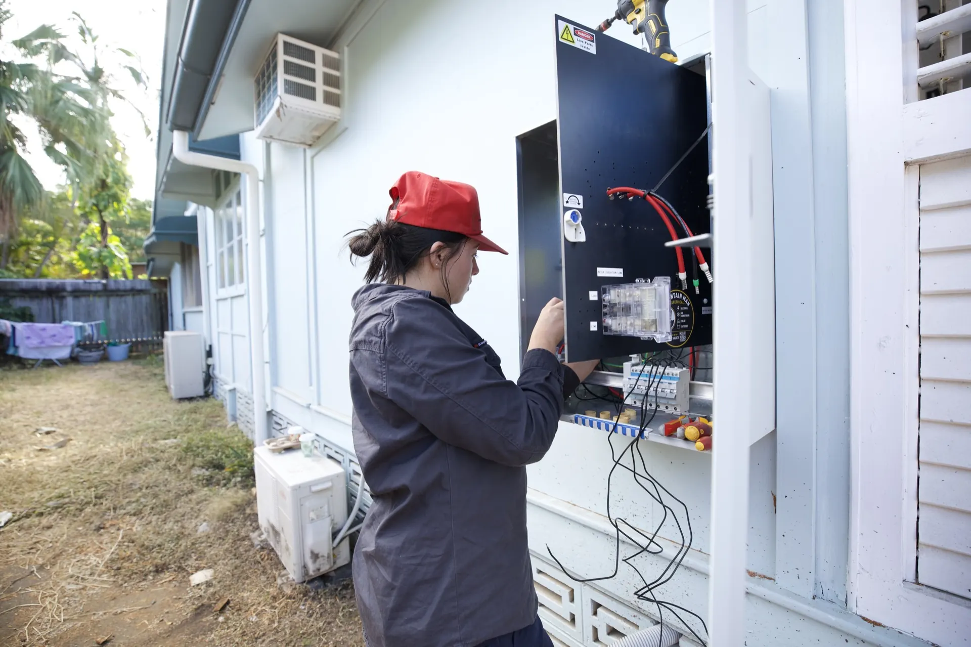 An electrician wiring the new meter board on the outside wall at the front of the house